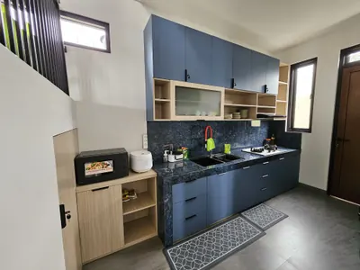 Dapur villa dengan kabinet biru, kompor, microwave, dan rak penyimpanan. Lengkap dengan peralatan masak dan perlengkapan makan.