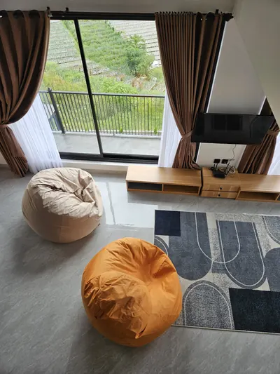 Sudut santai dengan bean bag menghadap jendela besar dan pemandangan perbukitan dan ladang.